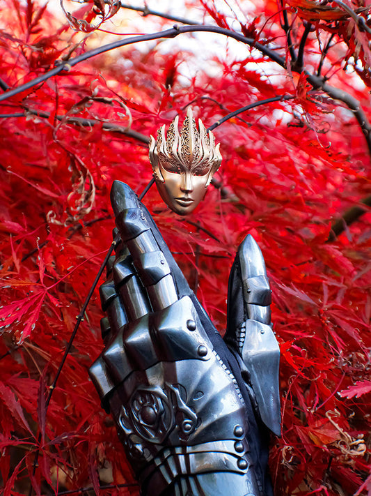 Hand wearing Phoenix Gauntlet reaching up to bronze Sovereign Brooch on maple leaf background